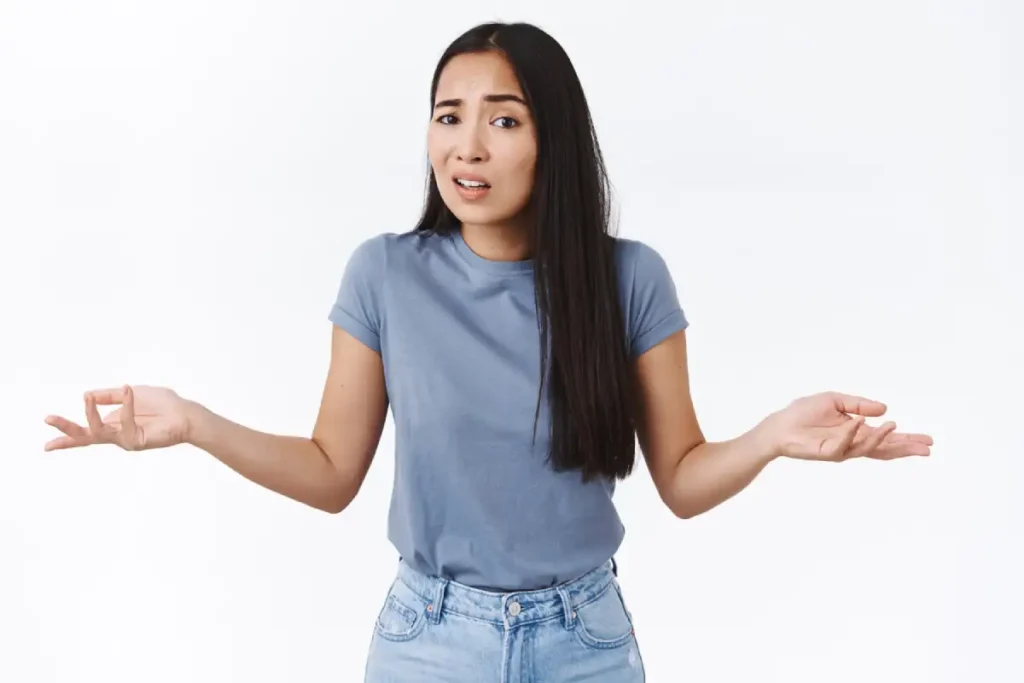 Asian girl worries about clinical trials, standing perplexed, shrugging with hands spread sideways in dismay