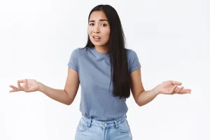 Asian girl worries about clinical trials, standing perplexed, shrugging with hands spread sideways in dismay